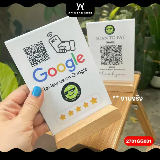 มือถือป้ายอะคริลิกสีขาวบนฐานไม้ พิมพ์ไอคอน NFC โลโก้ Google QR Code และดาวห้าดวง วางข้างป้ายสแกนจ่ายเงิน